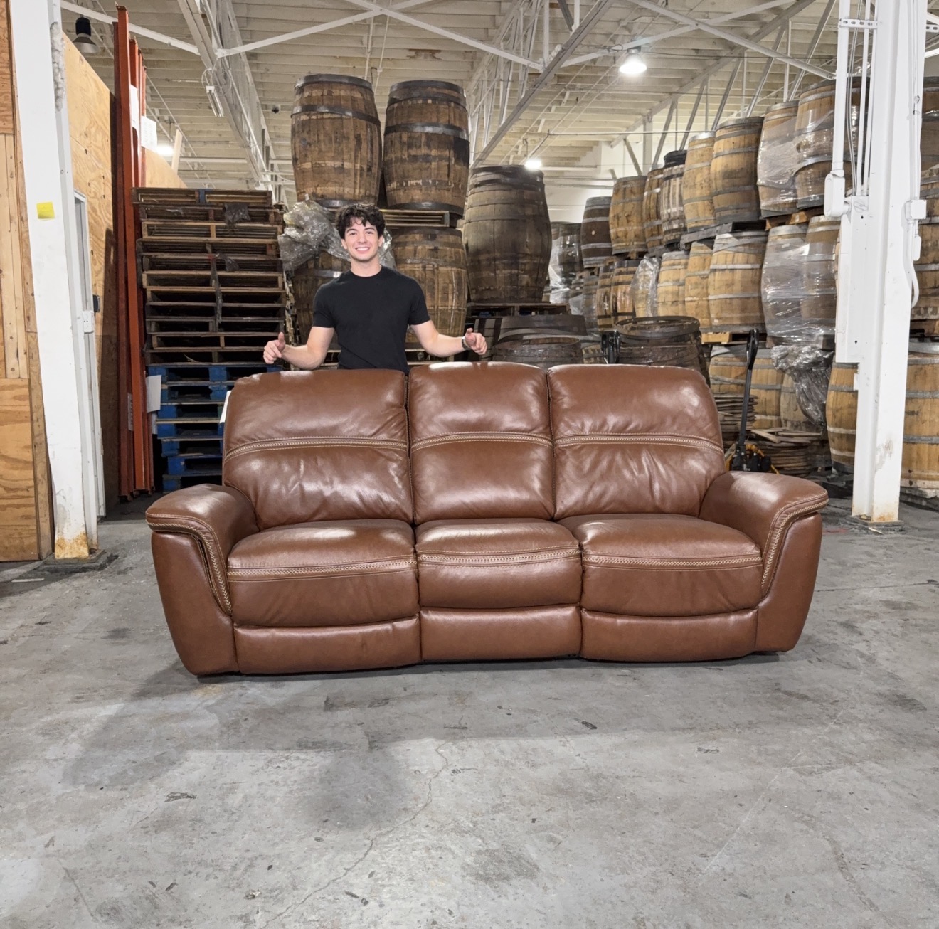 Julian smiling behind a brown leather sofa in the warehouse